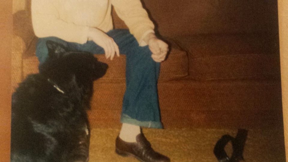 Old 110 photo that has been partially bleached away of a man sitting on an orange couch next to a dog. The man's head did not make it into the picture but the black dog looks great.