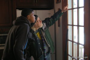 Workman and intern look out french doors at Keeler Gardens. Workman is pointing up towards the needed repair and intern is looking and listening intently.