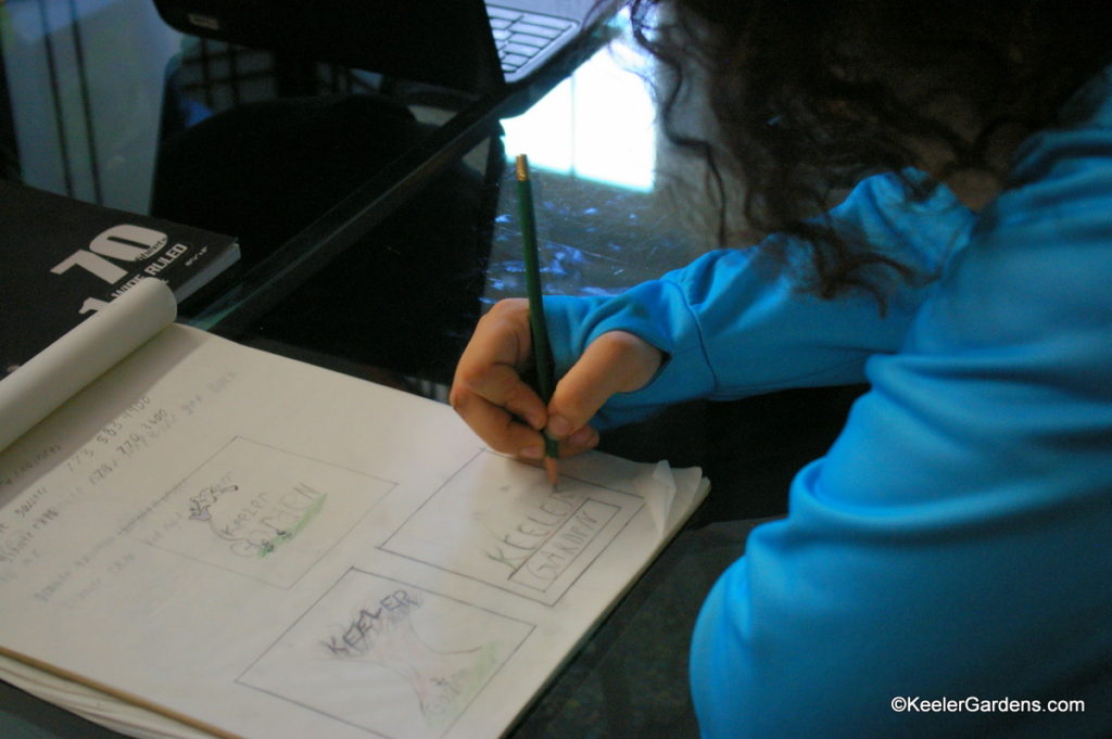 In his blue sweatshirt our art intern takes out a pencil and focuses sketches new ideas for a Keeler Gardens logo. Some of his designs incorporate Keeler Gardens name into nature, like the branches of trees or in a flower bed.